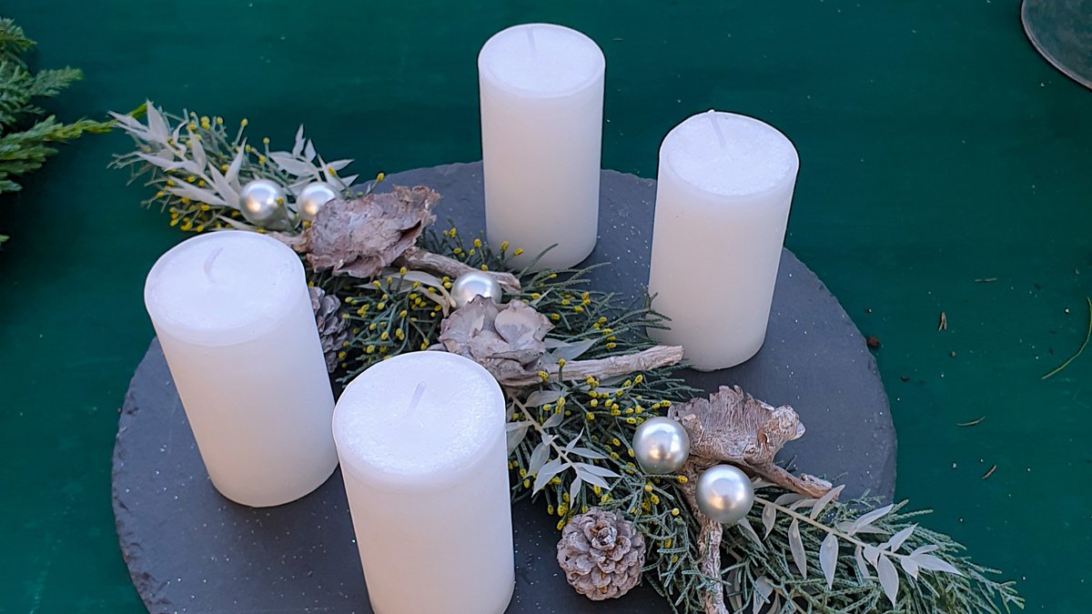 Minimalistische Adventsdekoration mit vier weißen Kerzen, kleinem Arrangement und Schieferplatte