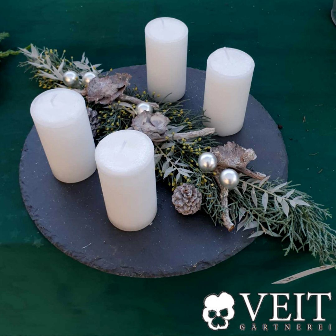 Adventsdekoration mit vier weißen Kerzen auf einer Schieferplatte