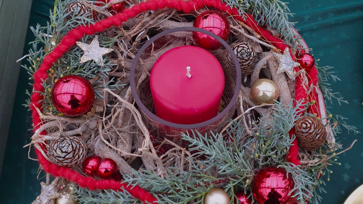 Adventskranz mit einer roten Kerze in der Mitte und roten Christbaumkugeln